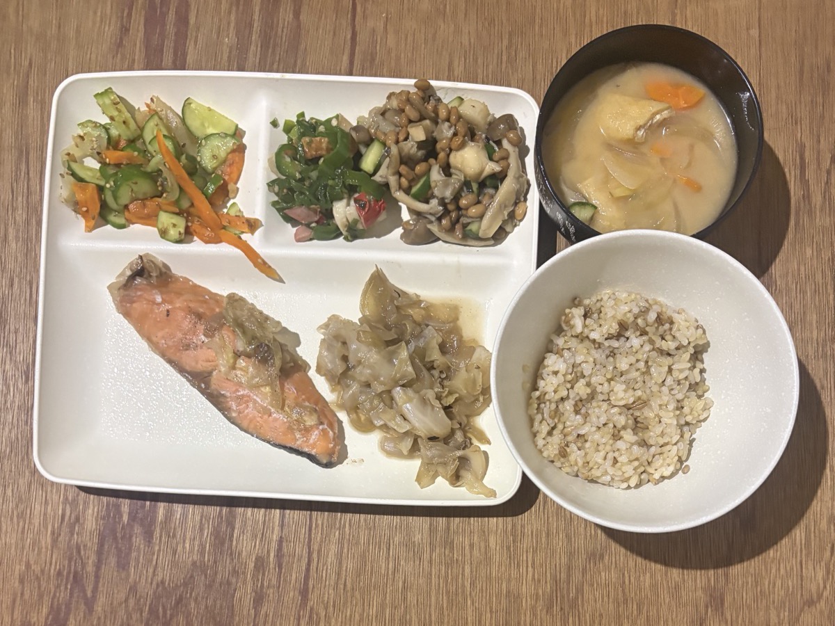 仕切りプレートに盛った焼き鮭とキャベツの炒め煮、きゅうりと人参の酢の物、ピーマンとわかめの和え物、しめじと大豆の煮物。具だくさんの味噌汁と玄米ご飯の茶碗